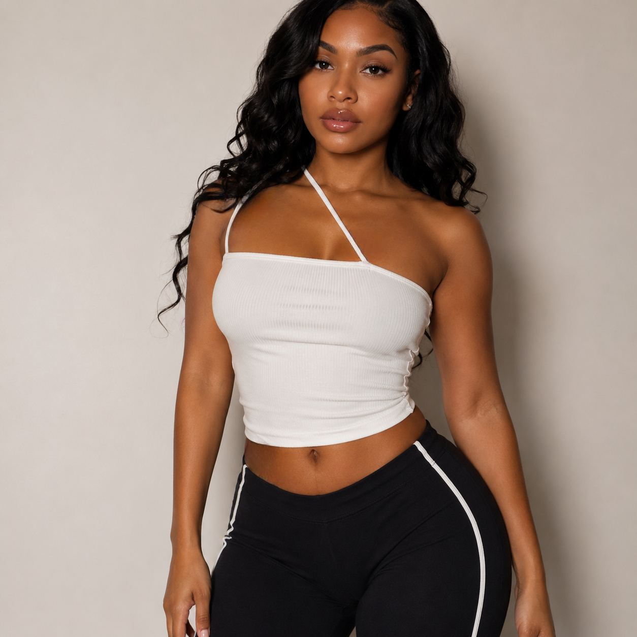 Woman wearing a white halter top and black pants with a white stripe against a neutral background
