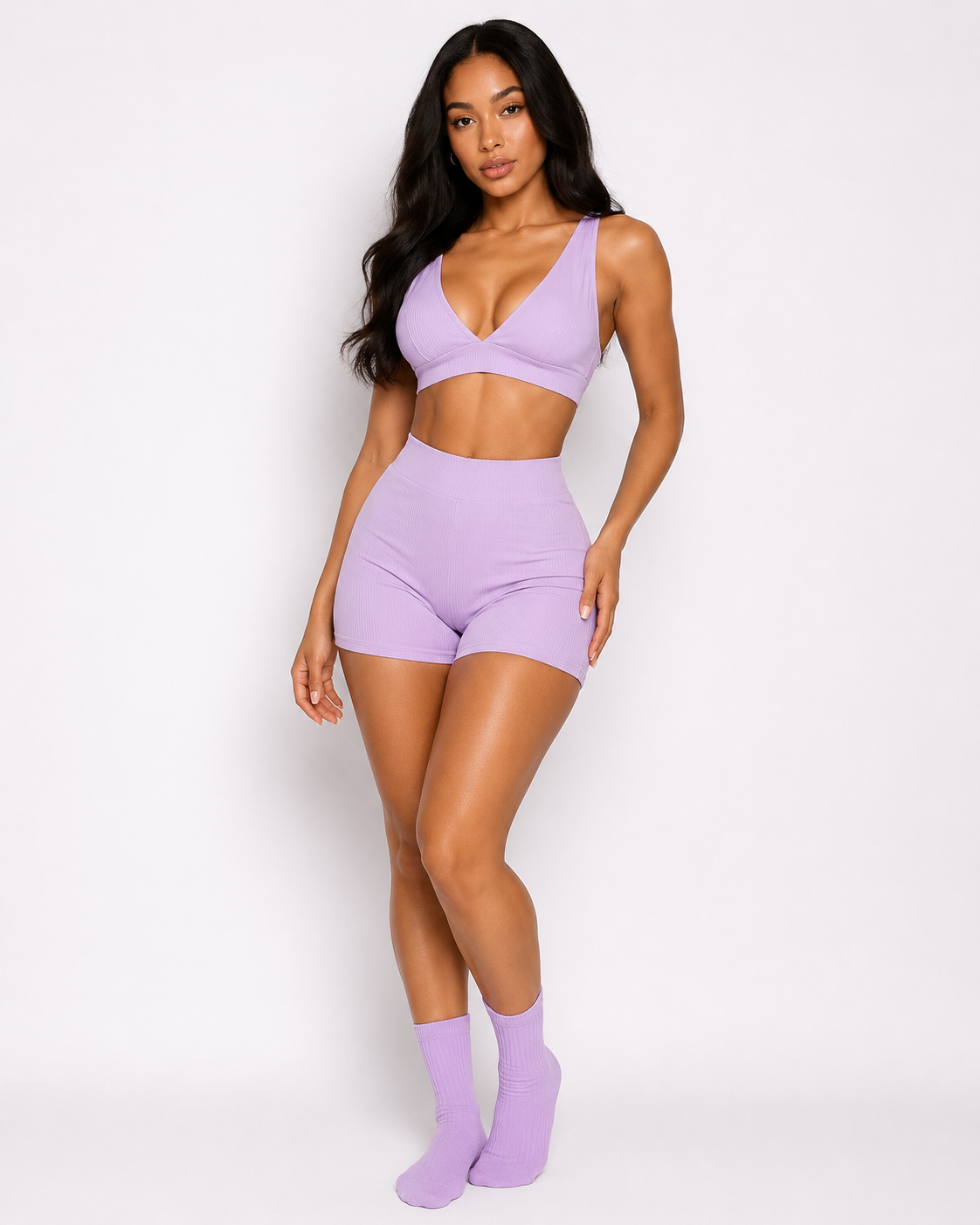 Woman wearing a lavender sports bra and shorts set with matching socks on a white background