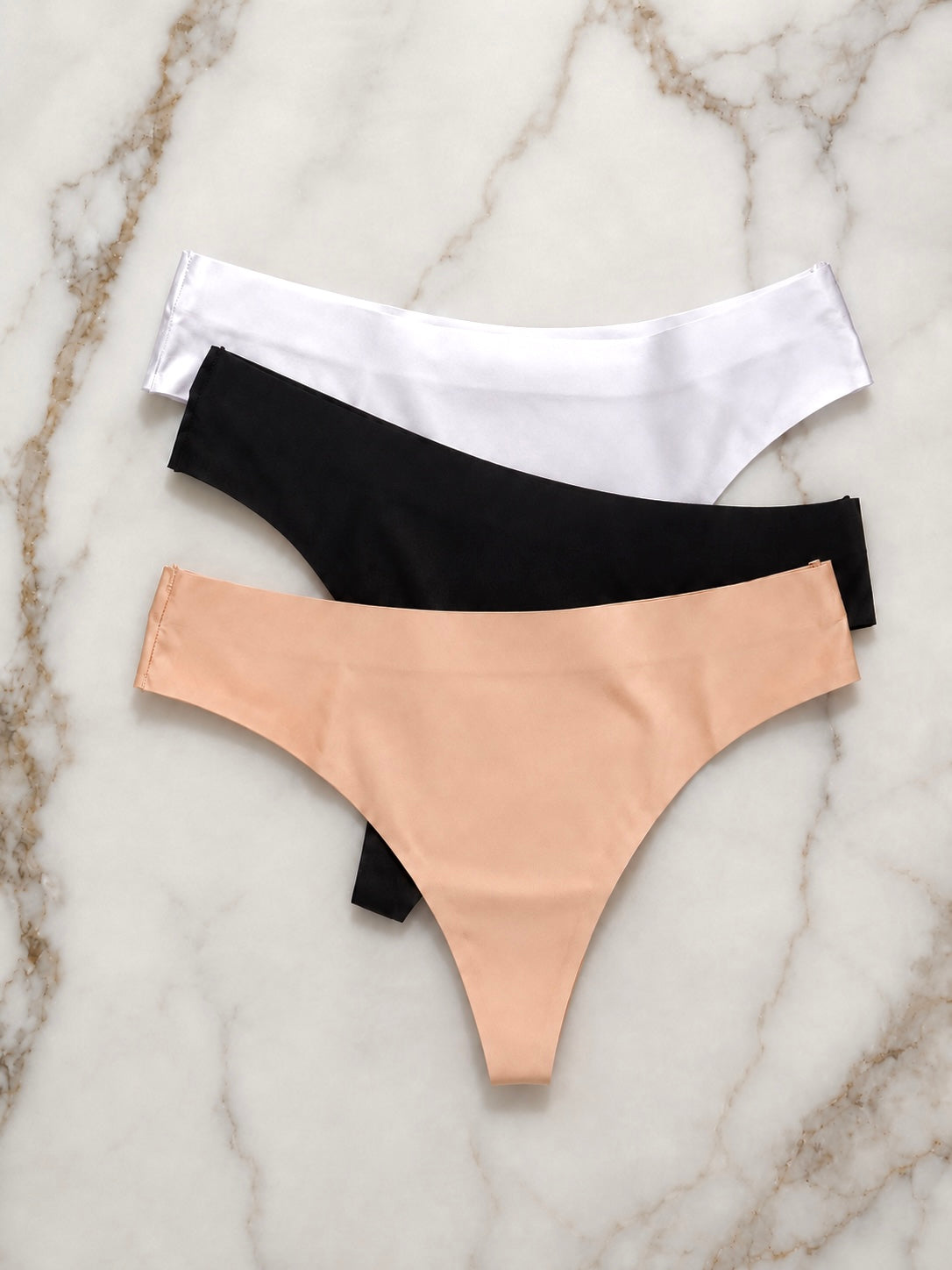 Three pairs of underwear in black, white, and beige on a marble surface.